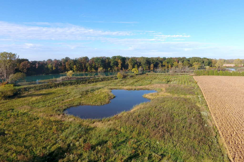 An aerial shot of a small pond in the middle of a rural farm setting.